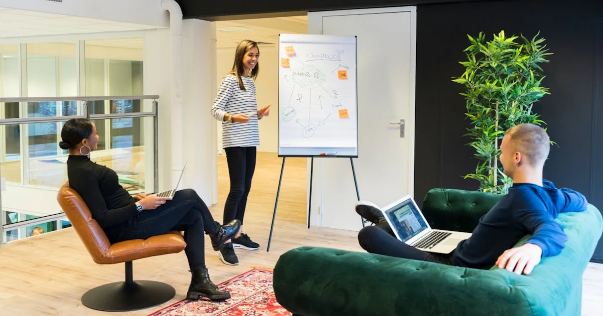 Two Person Listening to Woman Standing Beside Poster