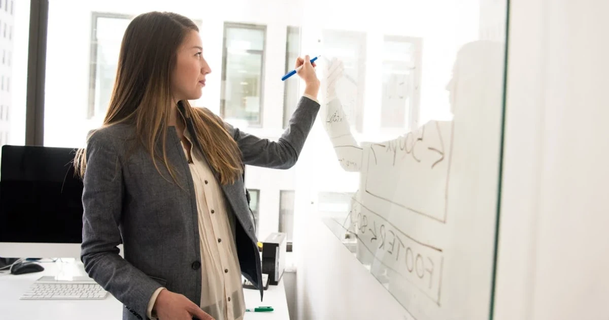 Woman Wearing Gray Blazer Writing on Dry-erase Board