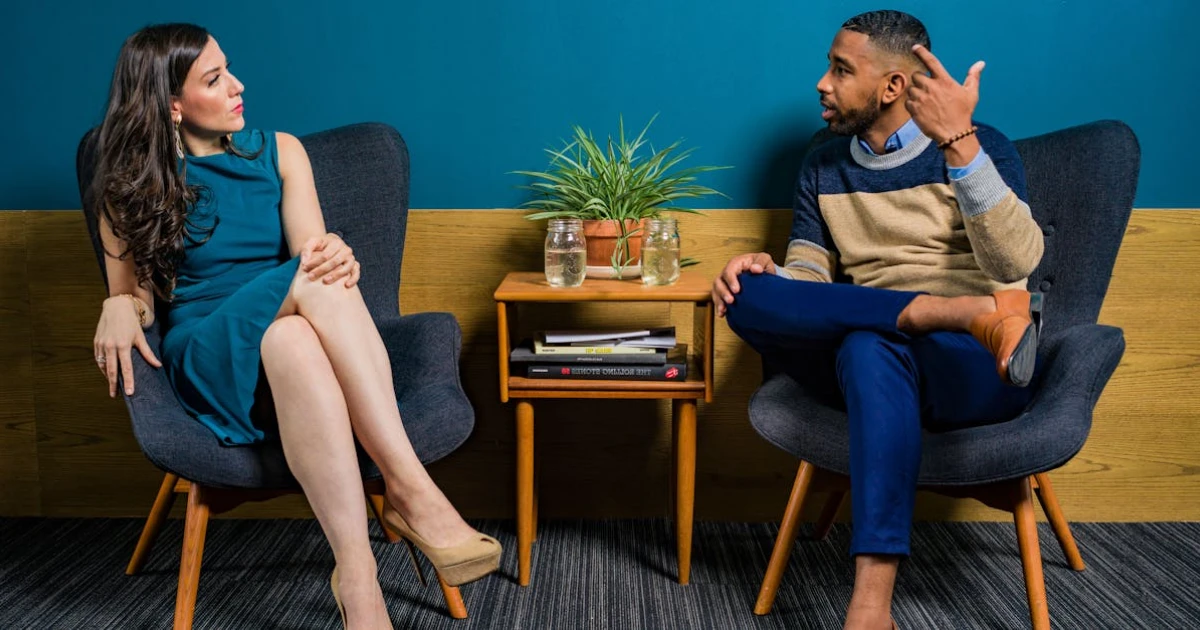 Woman Wearing Teal Dress Sitting on Chair Talking to Man